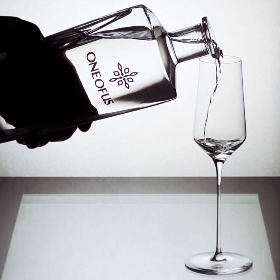 ONE OF US Mezcal bottle being poured into a fine glass on a white background