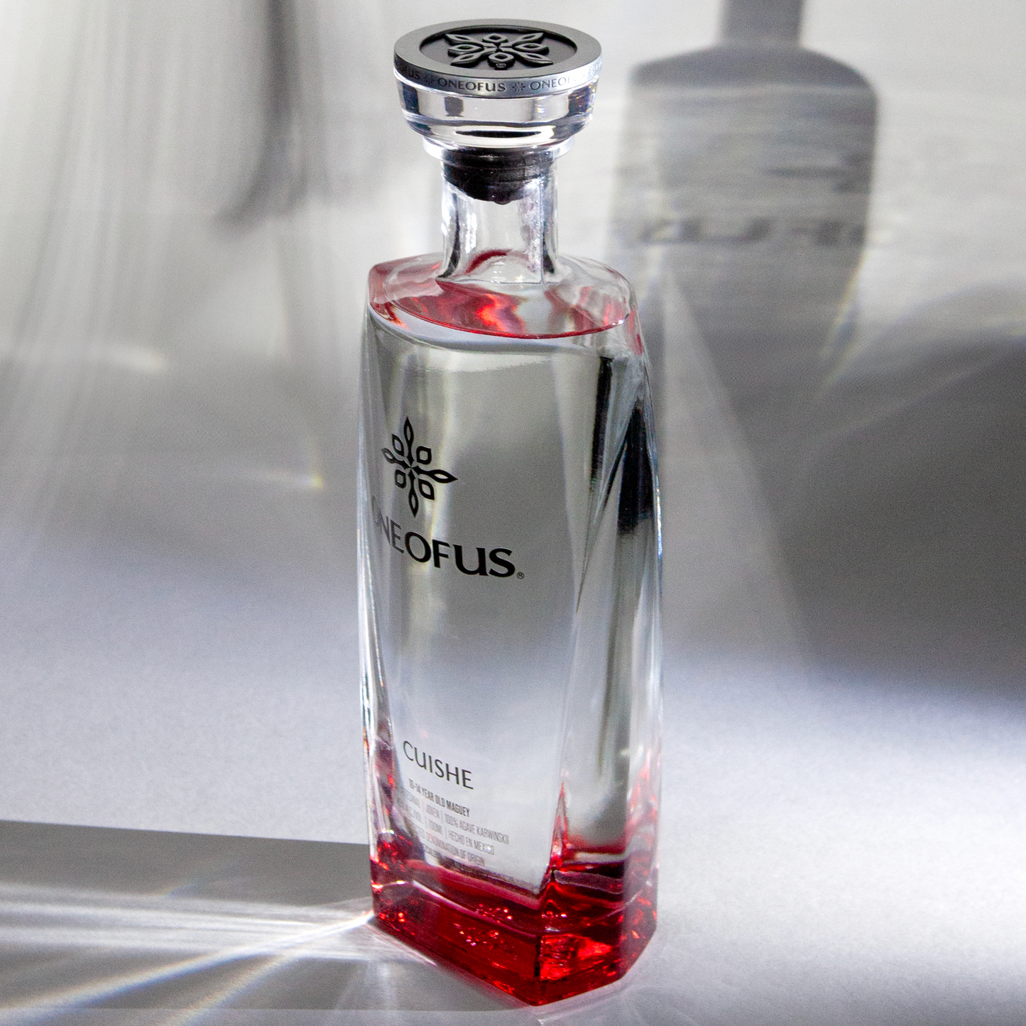 Clear glass bottle with red liquid and ONE OF US branding on a reflective surface.